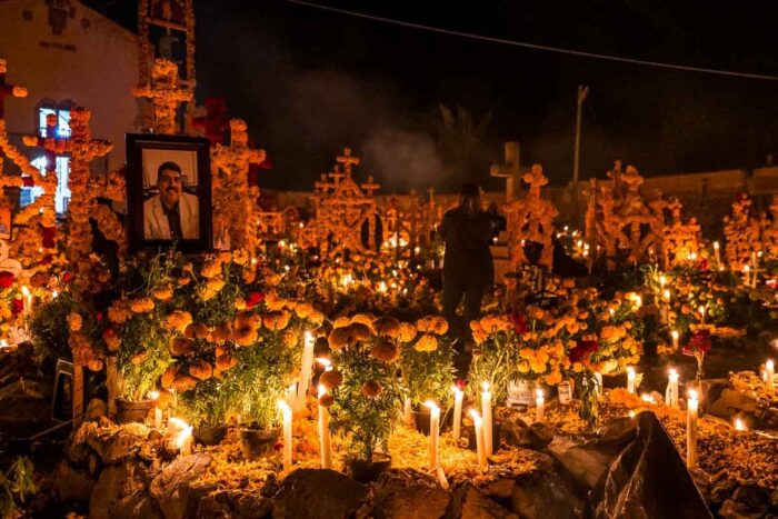 Close-up at night of burning candles and yellow flowers on the grave of a man whose picture is on the cross on the Day of the Dead in Patzcuaro.