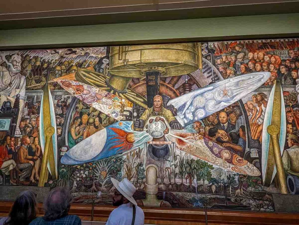 A colorful mural in Mexico City by Diego Rivera named 'Man the Controller,' showing a person surrounded by machines, with bright colors and lots of details.