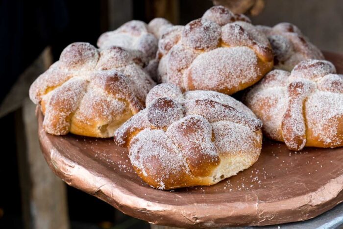 A close-up of a plate with about 6 pan de muertos topped with sugar on the Day of the Dead in Mexico