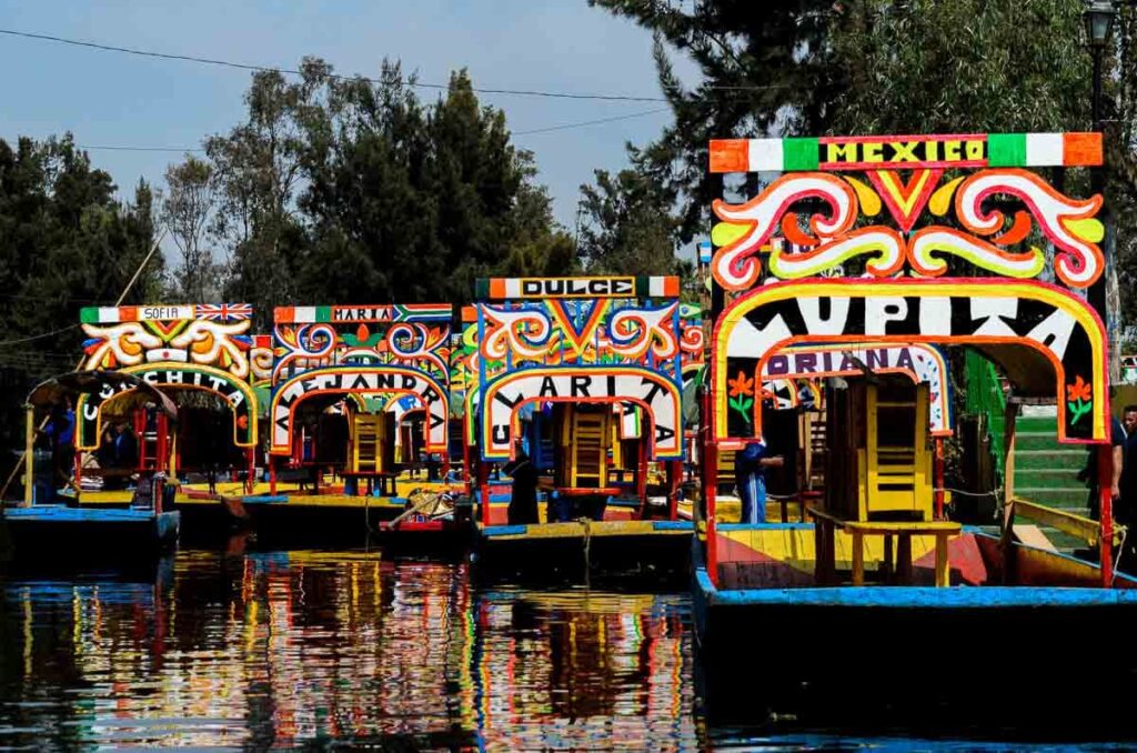 4 colorful boats or trajineras in Xochimilco each with their own name, such as "Lupita", "Clarita" and "Alejandra".