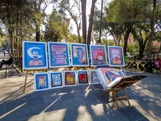 Outside of the Saturday market in San Angel, artwork is displayed on easels in the park.