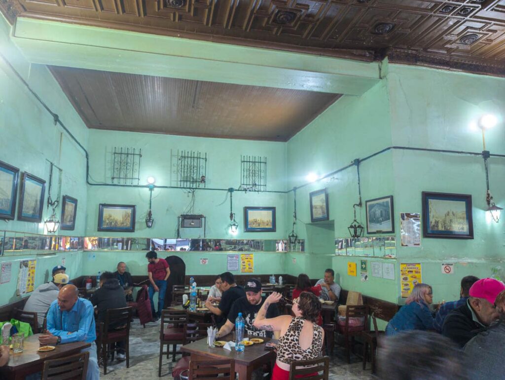 People sit a wooden tables inside Cantina La Dominica socializing and drinking beers.
