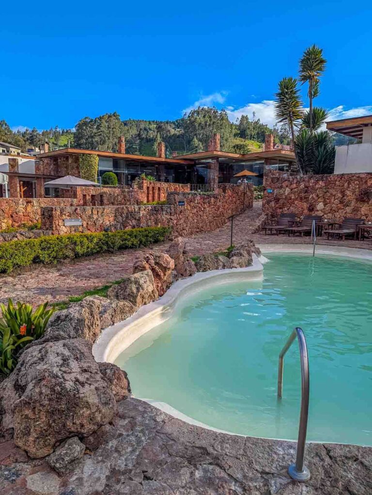 Curved mineral pool at Piedra de Agua hot springs in Cuenca Ecuador, nestled among stone landscaping with views of the spa buildings and Andean hills.