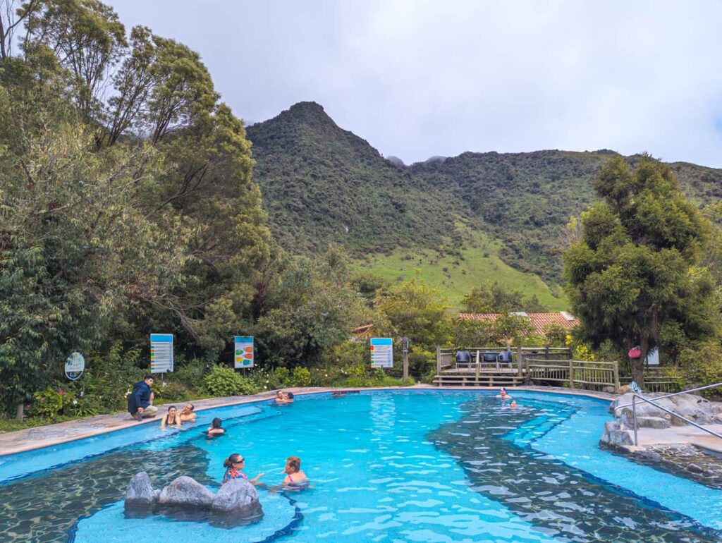 People soak in a large pool of hot springs at Papallacta resort near Quito. In the background are lush green mountains.