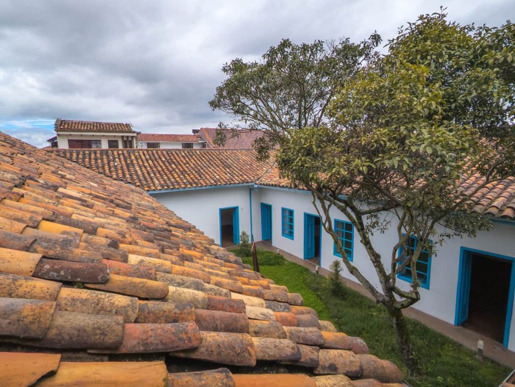 Traditional clay-tiled rooftops and a grassy courtyard with blue-trimmed doors inside a restored colonial building that houses one of the museums in Cuenca Ecuador.