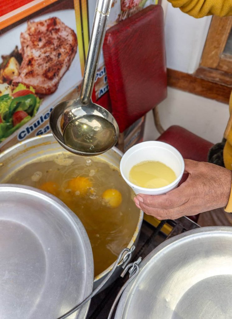 A vendor ladles canelazo, a hot traditional drink of Ecuador into a white cup near Quilotoa Lake.