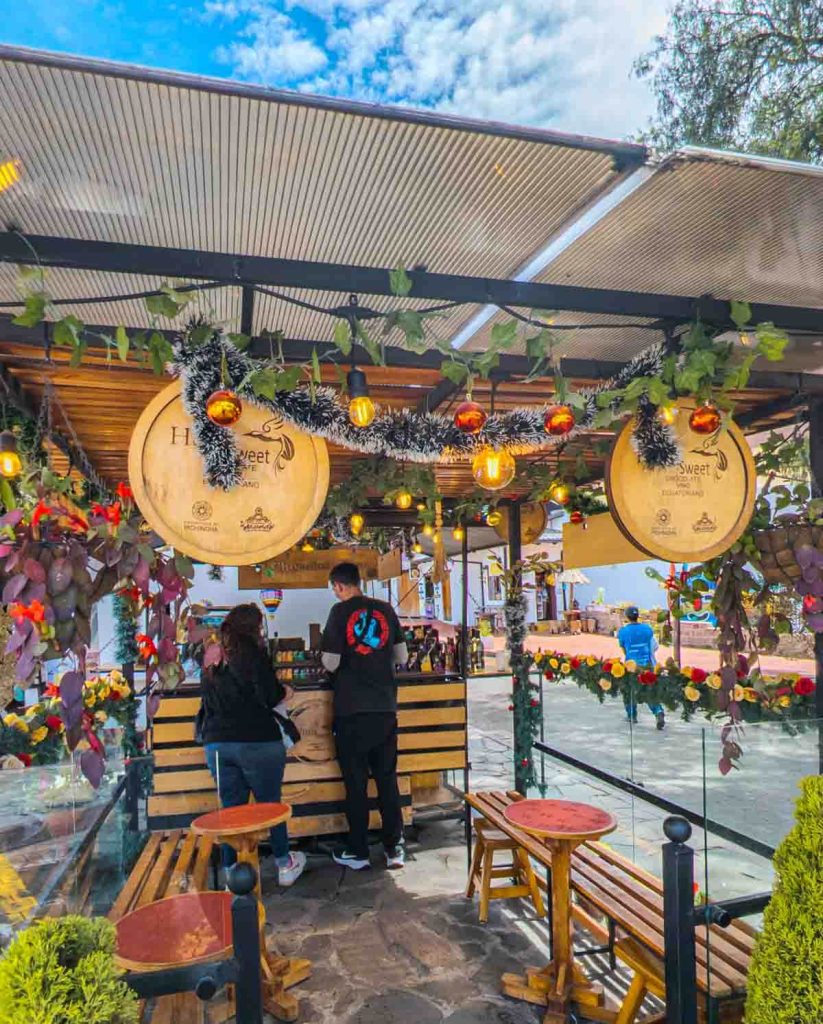 Visitors shop at a decorated outdoor chocolate booth inside La Ciudad Mitad del Mundo, Ecuador.