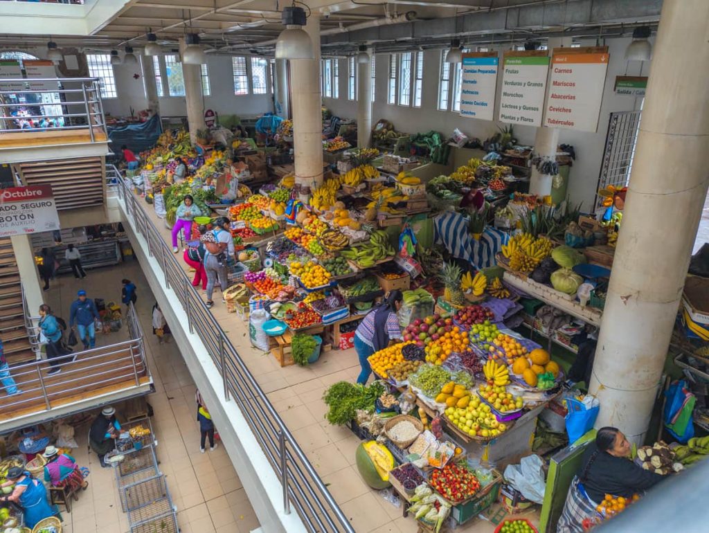 A vibrant upper-level view of Mercado 9 de Octubre in Cuenca Ecuador, showcasing colorful fruit and vegetable stalls and vendors.