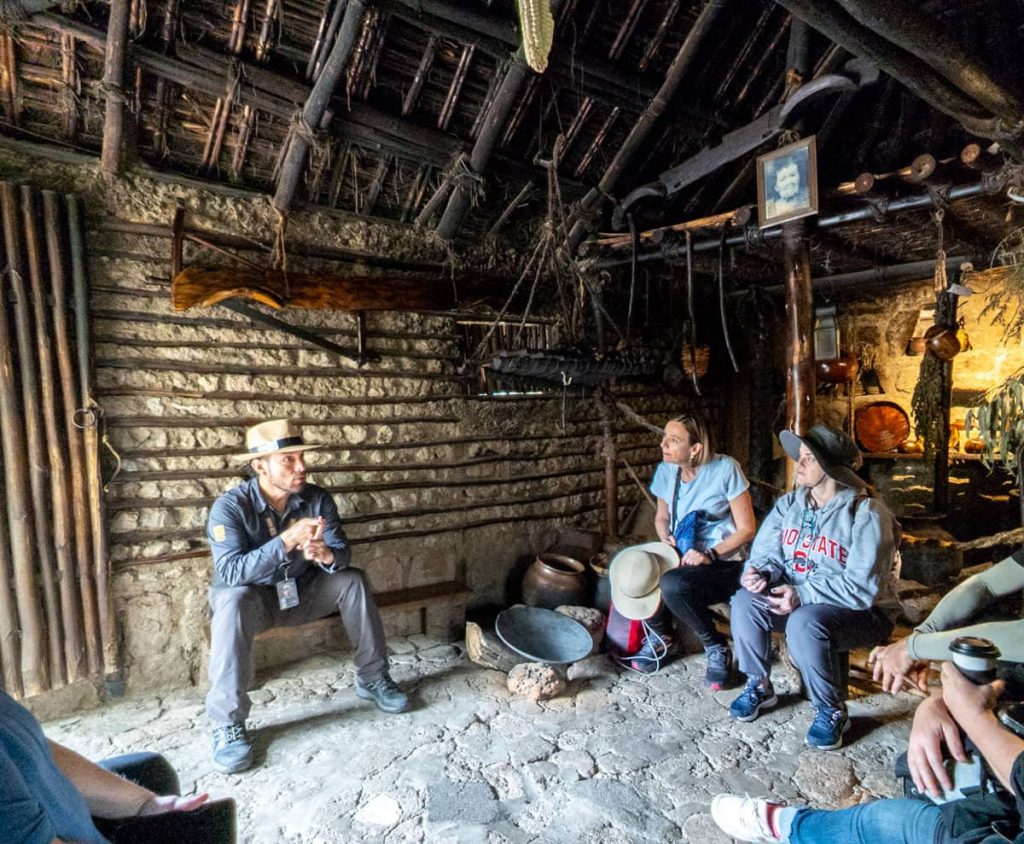 A tour guide explains indigenous traditions to a group of tourists sitting inside a reconstructed dwelling at the Intiñan Museum near the Middle of the World.