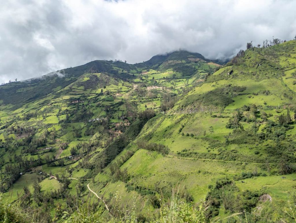 Lush green Andean mountains stretch into the distance under heavy cloud cover, showing typical landscapes on the Baños to Cuenca direct bus route.