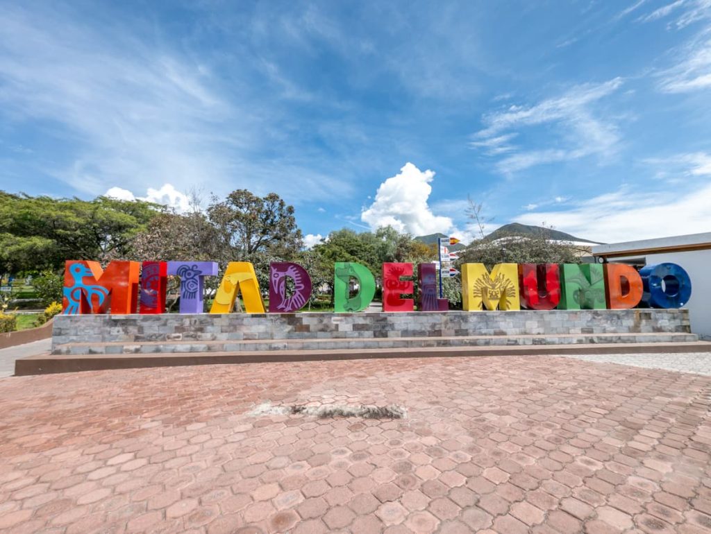 Bold, multicolored “Mitad del Mundo” sign on display at the main entrance of the city. It's a popular photo spot for visitors to the equator in Ecuador.