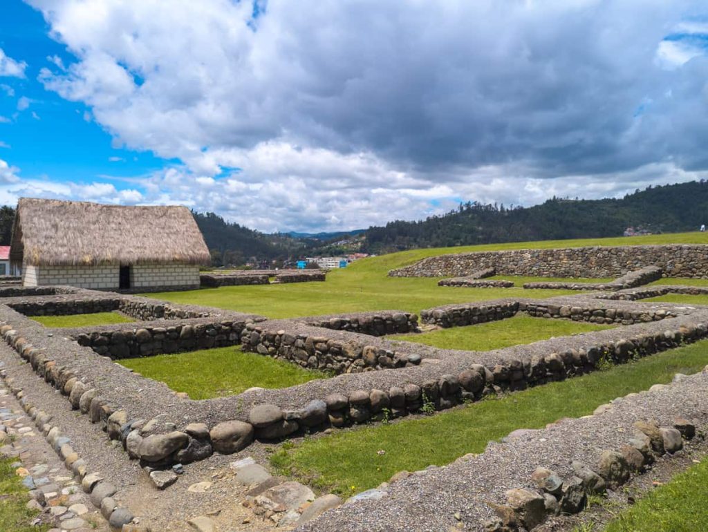 Stone foundations and reconstructed thatch-roofed building at the Pumapungo ruins in Cuenca Ecuador.