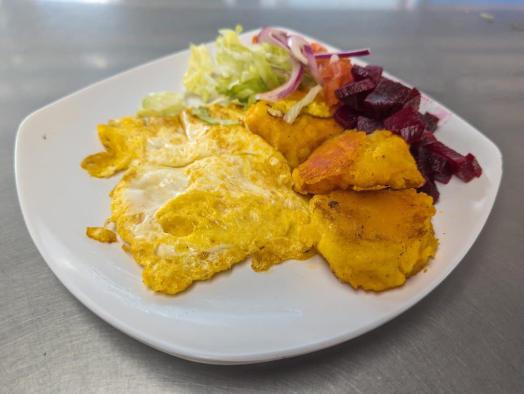 A white plate llapingachos, a typical Ecuadorian food made of mashed potatoes and cheese. It's served with eggs, salad, and beets.