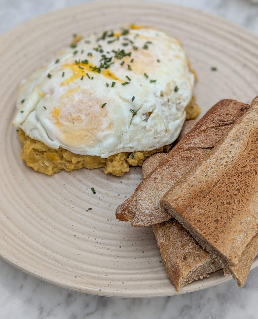 A plate of tigrillo topped with two fried eggs and served with crusty bread slices. Made from mashed green plantains and cheese, tigrillo is a beloved breakfast dish in Ecuador.