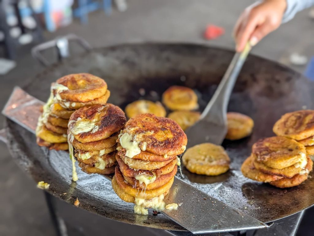 Stacks of freshly griddled tortillas, a street food in Ecuador, sizzling on a large hot plate, with melted cheese oozing between the golden-brown layers as a vendor flips them.