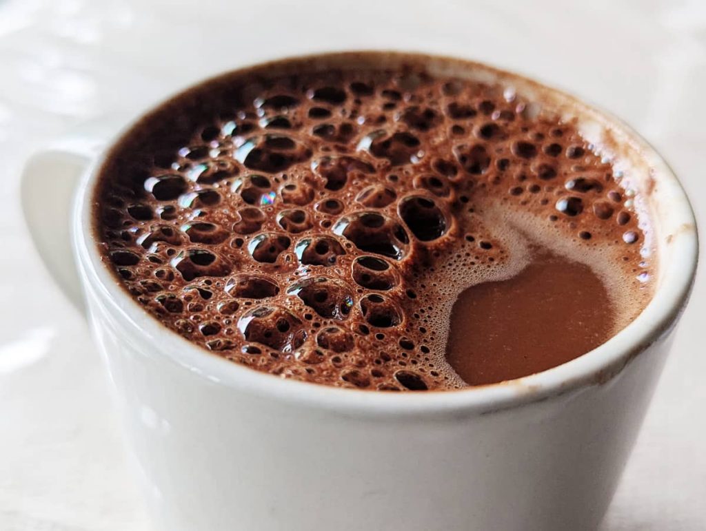 A close up of a white mug filled with a frothy hot chocolate drink in Mexico. Dozens of bubbles sit on the surface.