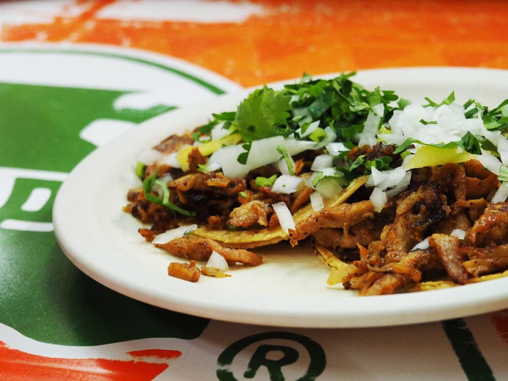 A white ceramic plate of grilled meat tacos on double corn tortillas topped with onion and cilantro.
