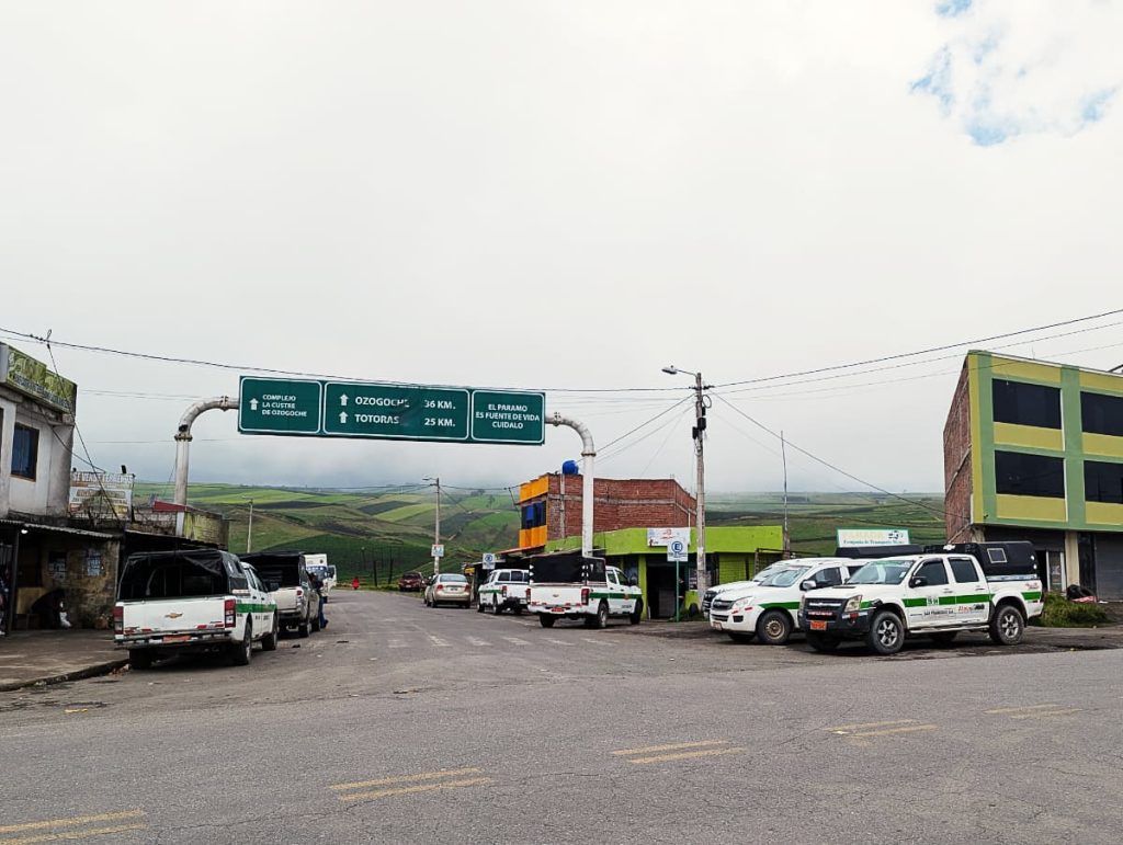 White pickup trucks with a green stripe wait along a highway junction at the turnoff for Lagunas de Ozogoche.