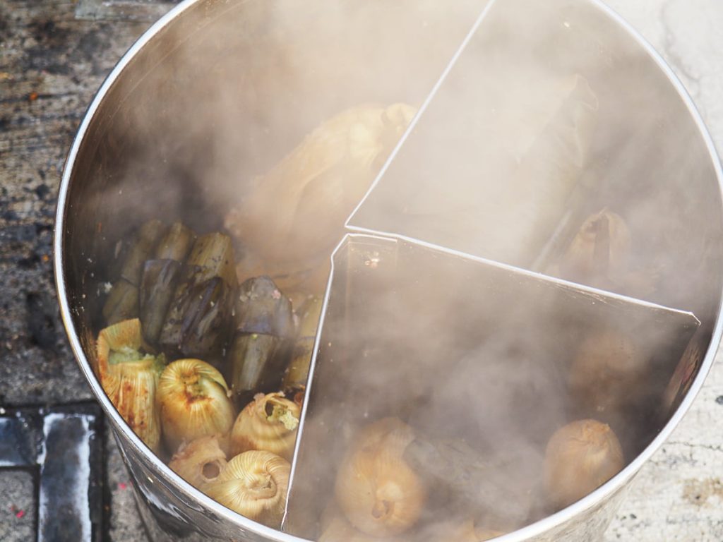 Steam rises from a divided stainless steel pot holding corn husk tamales and darker leaf-wrapped tamales, a typical breakfast in Mexico