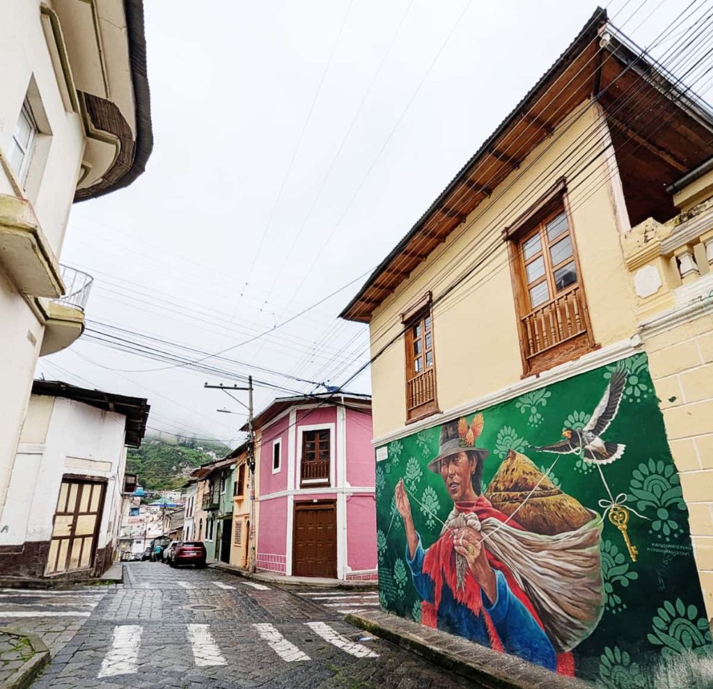 A striking mural in Alausí of a figure in traditional dress holding a string looped around a soaring condor with a key at the end on a yellow building.