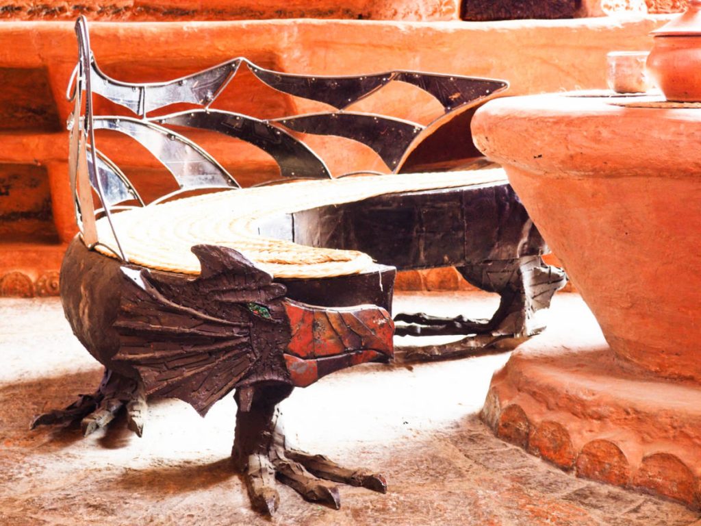 A dragon's face and body forged in metal form a bench around the clay table at Casa Terracota. The dragon's mouth is painted red while the eye is green and the feet of the dragon are the feet of the bench.