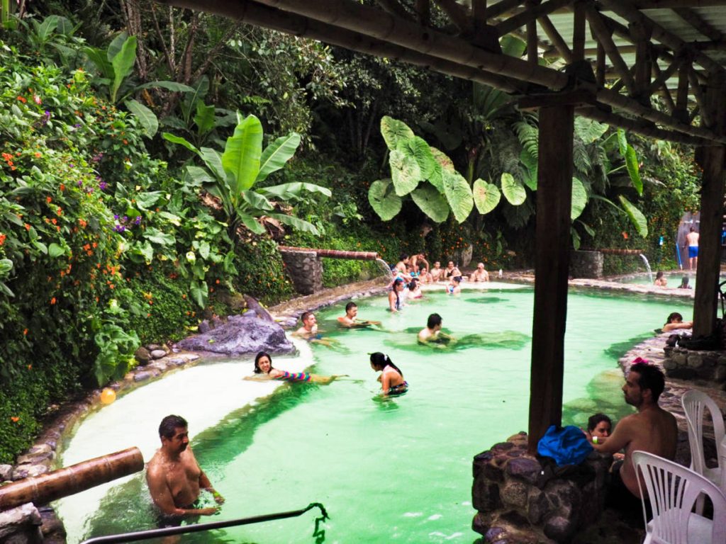 People soak in waist deep thermal water in Manizales. The water is a beautiful shade of green with tropical plants surrounding.