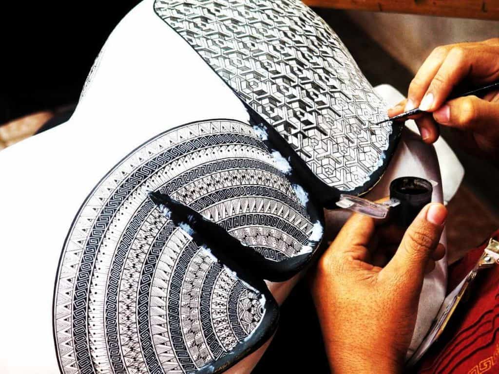 An artist paints the intricate details of an alebrije in a black and white Escher motif.