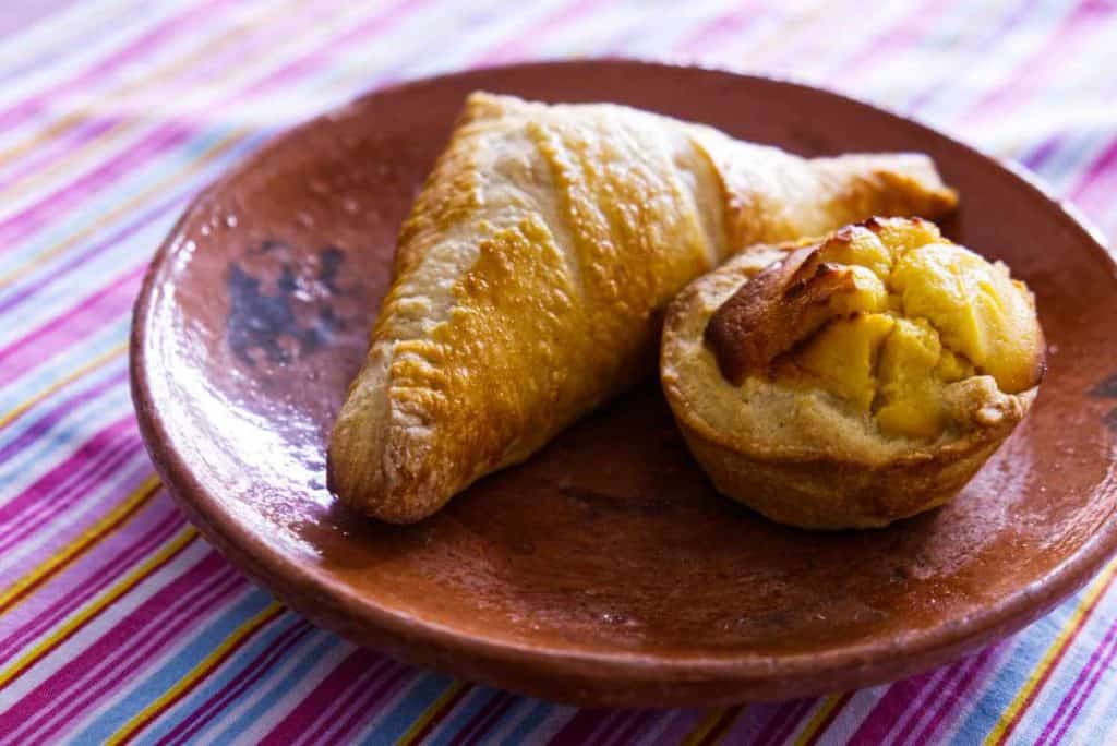 Two baked goods sits on a clay plate at Suenos Bakery in San Cristobal. A savory one of ham and cheese is in the shape of a triangle, next to a circular cheese bread.