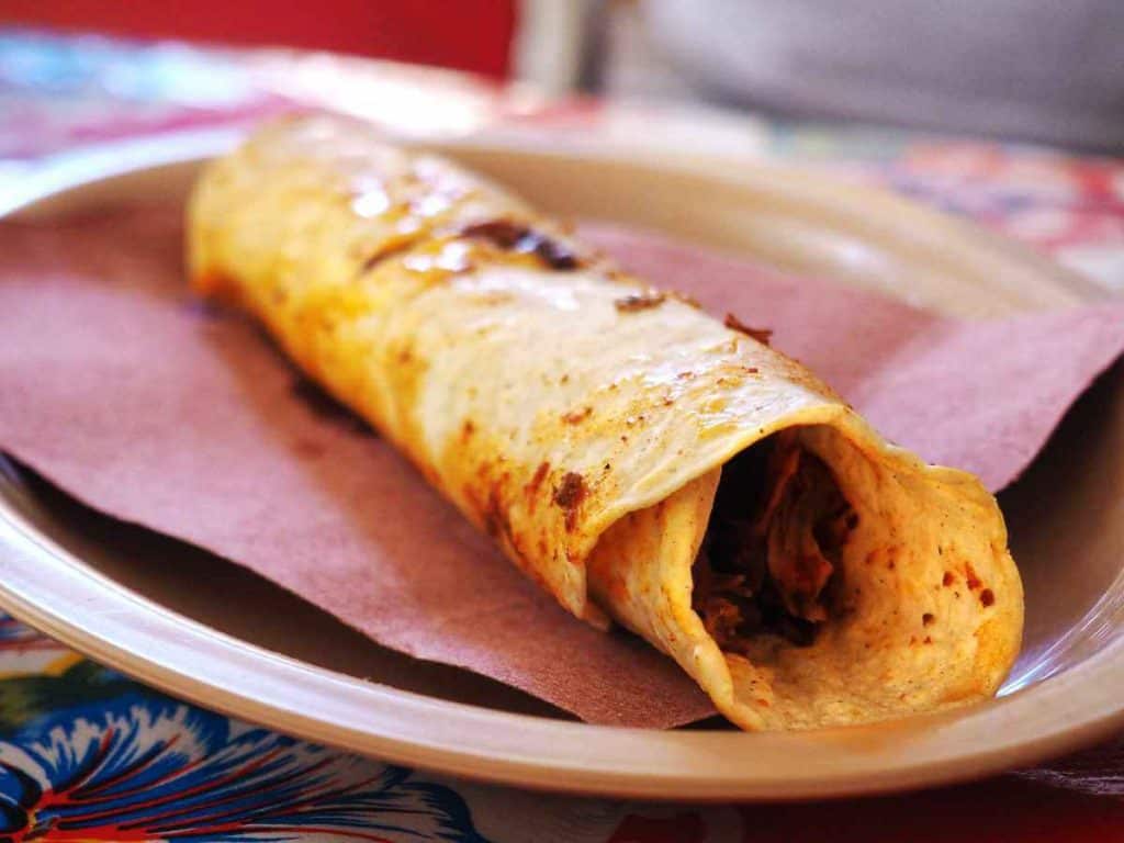 Barbacoa meat wrapped in a corn tortilla and served on a paper lined plate at the Tlacolula Market in Oaxaca.