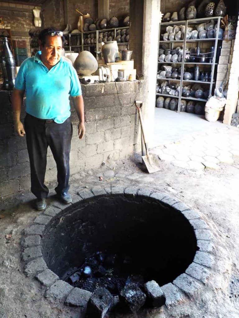 Fabian stands on the edge of the black pottery kiln which is dug into the ground and lined with bricks.