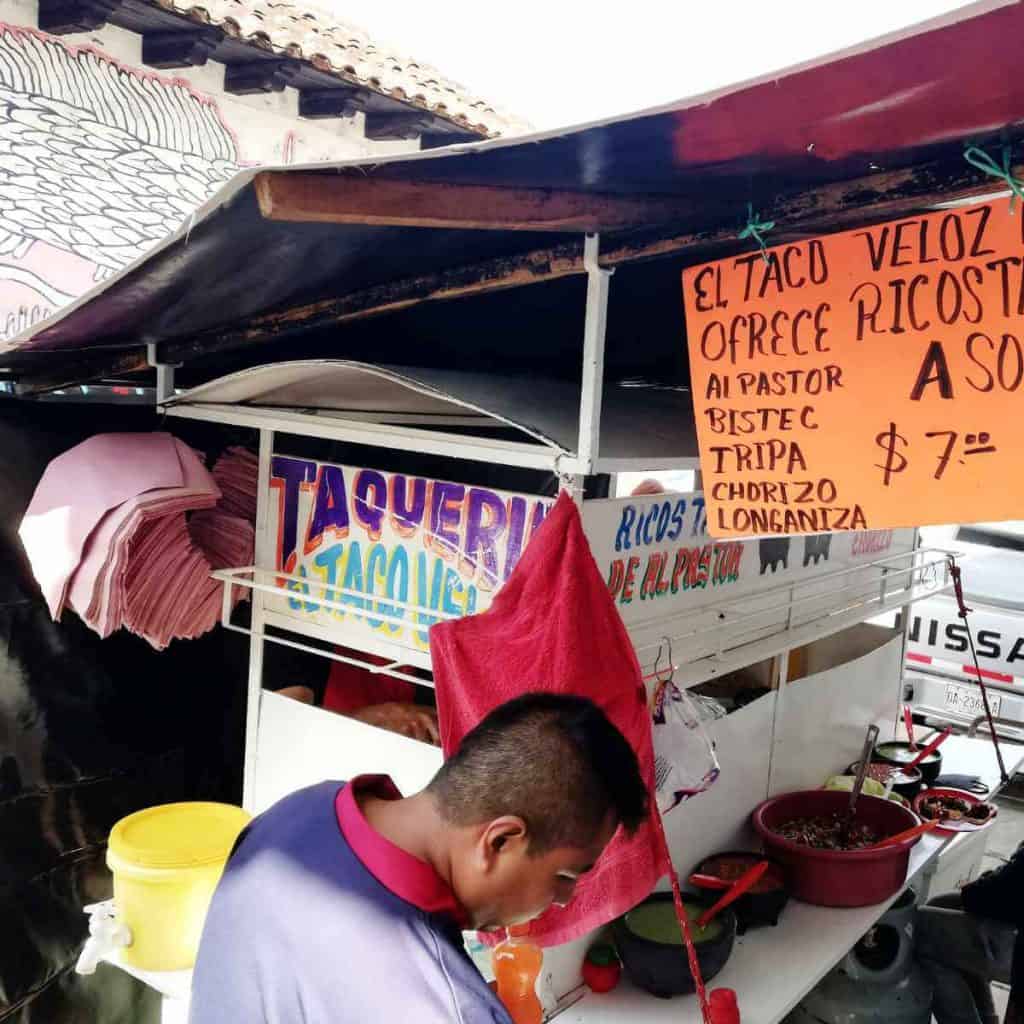 Some of the best tacos in San Cristobal can be found at this street cart which is white and colorfully painted Taqueria El Taco Veloz. An orange sign with hand-painted lettering advertising seven peso tacos hangs on the right.