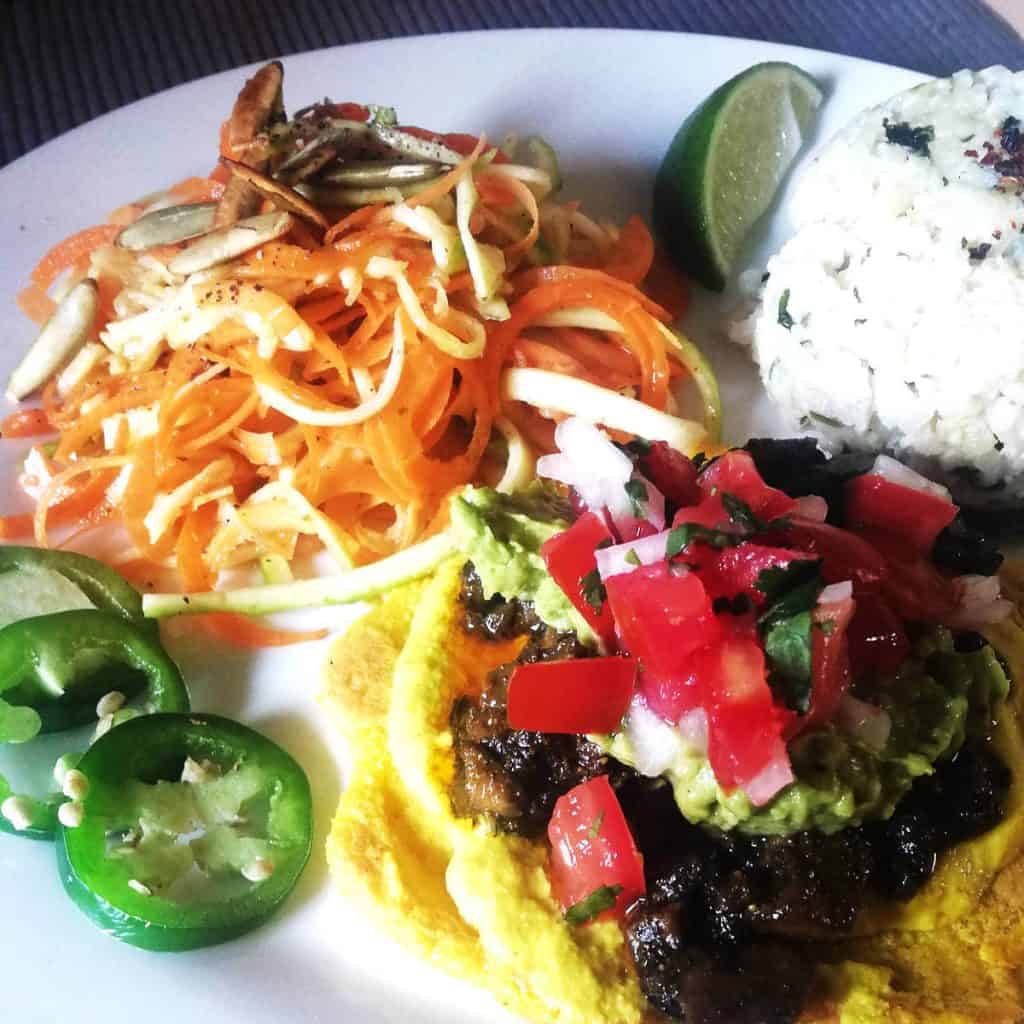 A vegan plate of tostadas topped with sautéed mushrooms, guacamole, and fresh salsa at La Cocina Consciente, one of the best vegan restaurants in San Cristobal de las Casas. The plate is accompanied by a salad of julienned carrots and zucchini topped with pumpkin seeds and a side of rice.