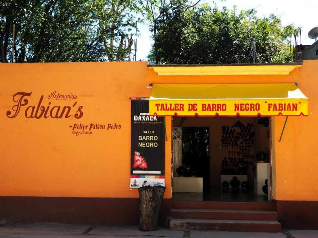 A bright orange building labeled Taller de Barro Negro "Fabian" welcomes visitors to the black pottery workshop in San Bartolo Coyotepec.