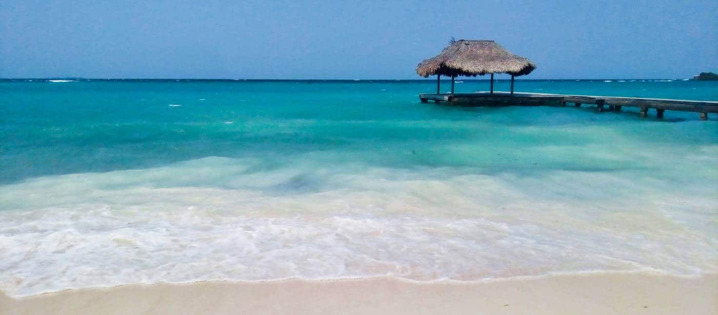 Surf comes onto the shore as a dock stretches into the turquoise sea on Isla Grande.