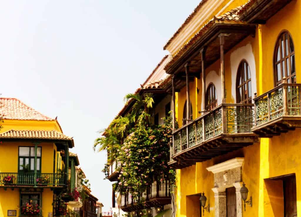 One of many colonial buildings in Cartagena's walled city, featuring a bright yellow facade and balconies spilling over with large tropical plants.