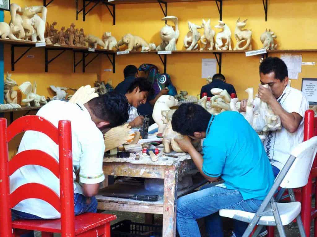 Workers sit at a communal table to carve alebrijes from copal wood during an alebrije tour of Taller Jacobo y Maria Angeles.