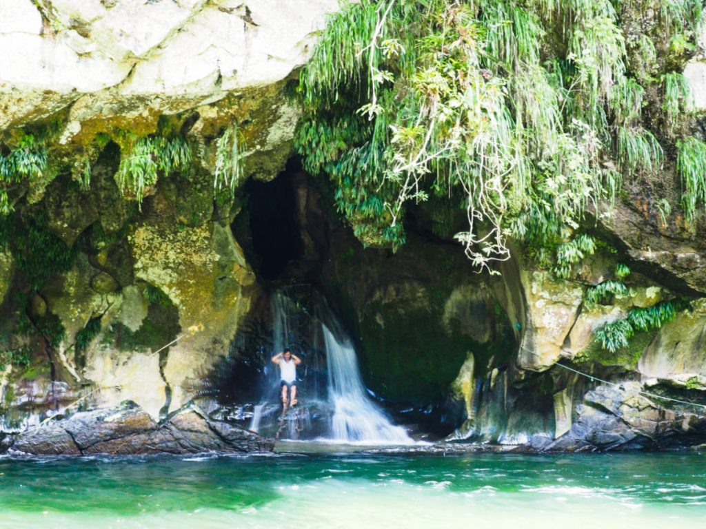 At the opening of the limestone cave, a man sits on the rocks to refresh in the spring that flows into Rio Claro at Playa Manantial.