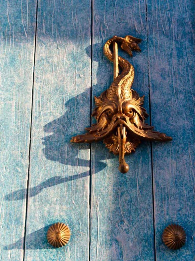 A metal sea creature door knocker on a weather turquoise door in Cartagena.