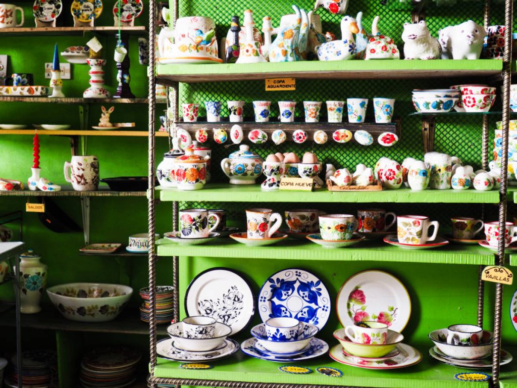 Various colorful hand painted ceramics line bright green shelves at a workshop in El Carmen de Viboral, one of several day trips from Medellin.