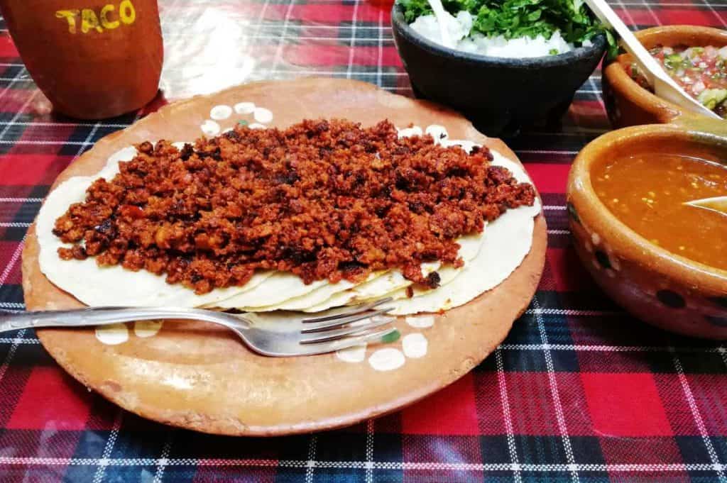 A pile of chorizo sits atop six tortillas which are layered on a traditional clay plate. Also on the table are a trio of salsas, which rounded out some of the best tacos in San Cristobal.