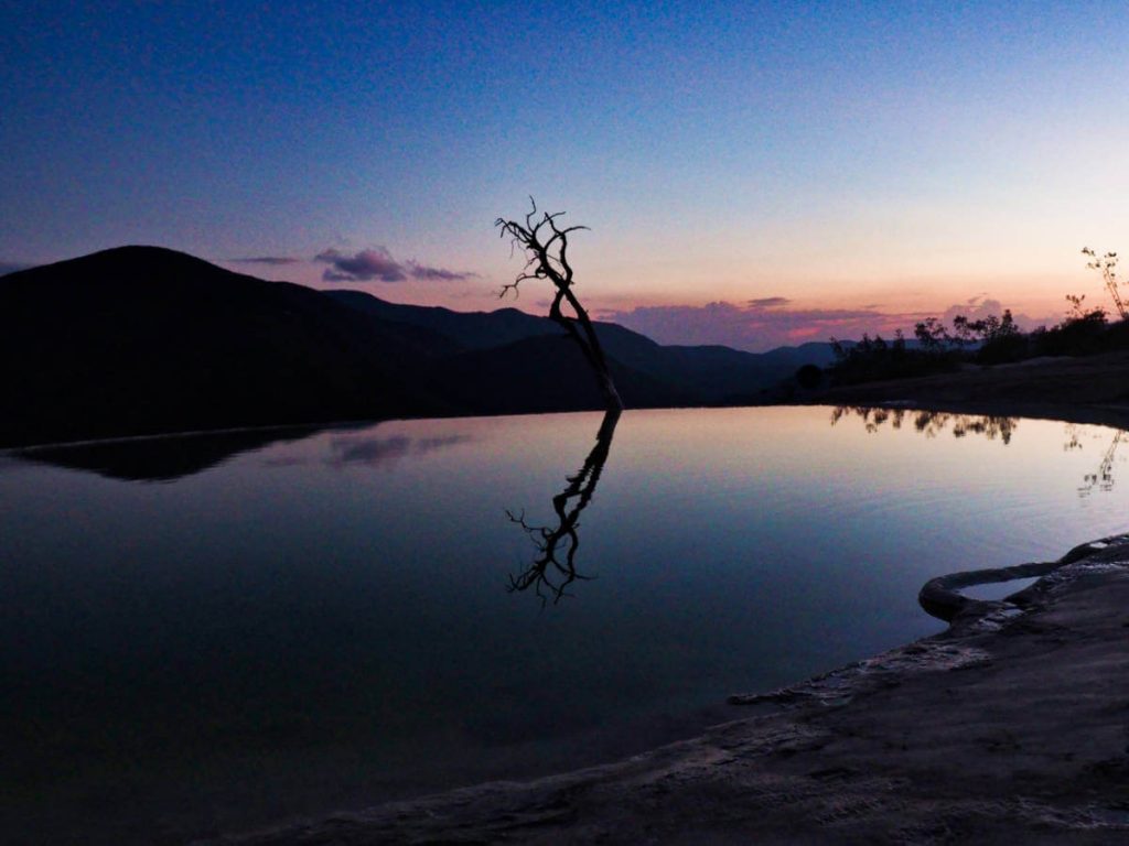 Silhouette of the infinity pool, tree, and surrounding mountains at sunset in Hierve el Agua, Oaxaca,