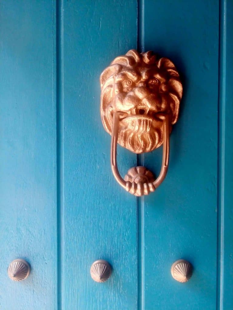 A metal lion's face door knocker on a turquoise door in Cartagena, Colombia.