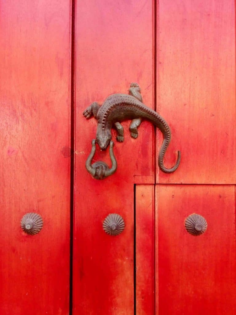 A metal lizard door knocker hung on a red door in Cartagena.