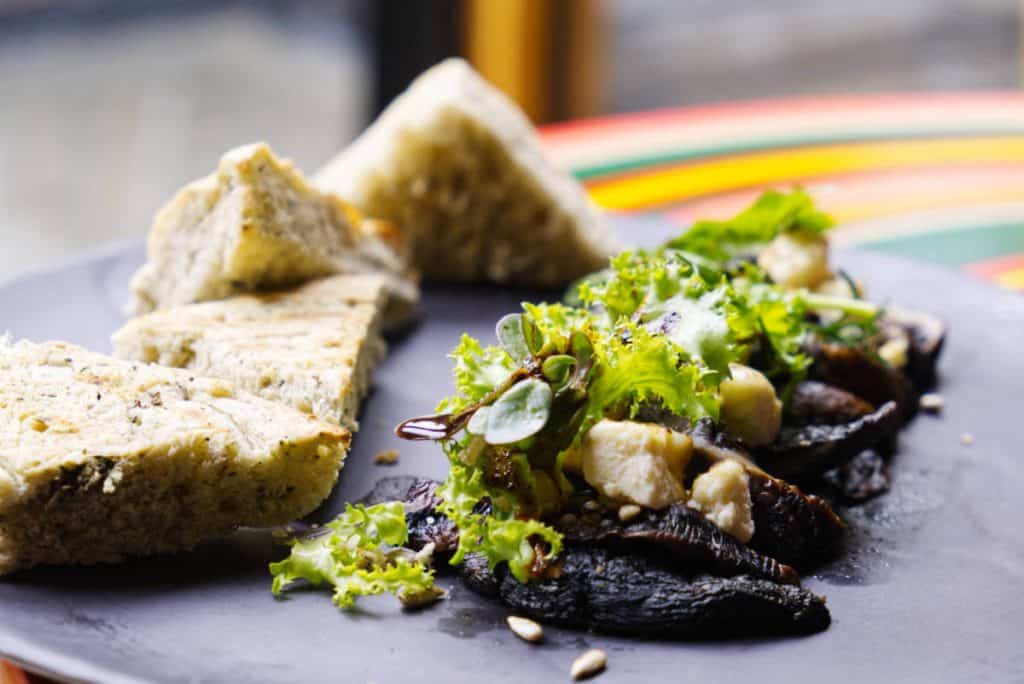 At Lum Restaurant in San Cristobal, an appetizer plate of marinated portabella mushrooms topped with fresh baby green, goat cheese, and sunflower seeds are accompanied by triangles of toasted focaccia bread.