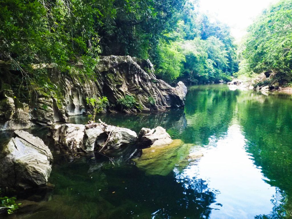 Rocks sculpted by the elements protrude from the water at Rio Claro near Medellin Antioquia. The river is surrounded by lush trees.