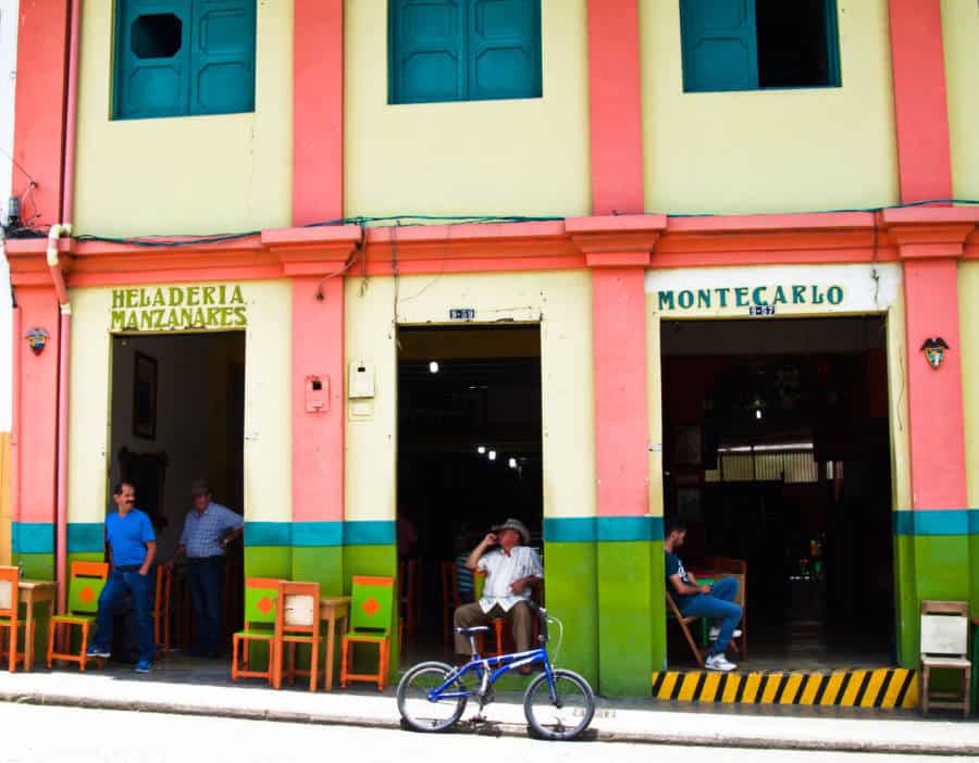 Men hang out in the large rectangular doorways of this brightly painted facade in Jardin, one of the most popular Medellin day trips.
