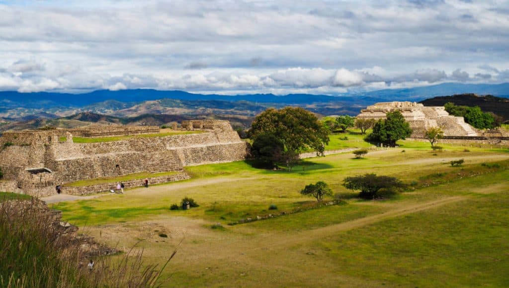 A landscape view of several buildings at Monte Alban with views of the mountains and Oaxaca valley in the background.