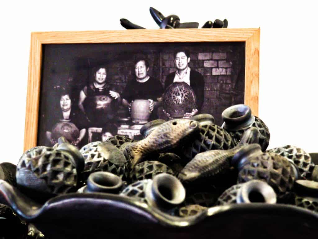 A family portrait of black pottery artisans is displayed in front of a bowl of small pottery pieces.