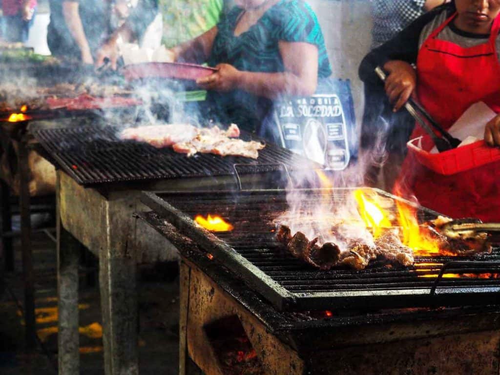 Woman tend to meats on the grill at Tlacolula Market.