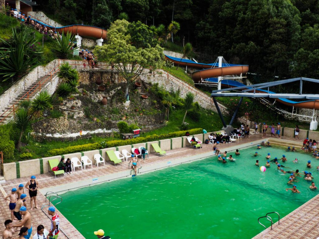 At the termales in Paipa, kids surround the thermal pool with a long line at the large slide behind.